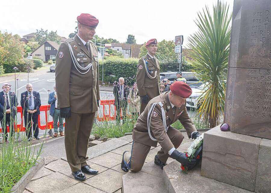Military personnel in uniform, with one kneeling to lay a wreath at a Polish memorial stone, surrounded by a small group of people in an outdoor setting - Fife-founded Polish parachute brigade commemoration