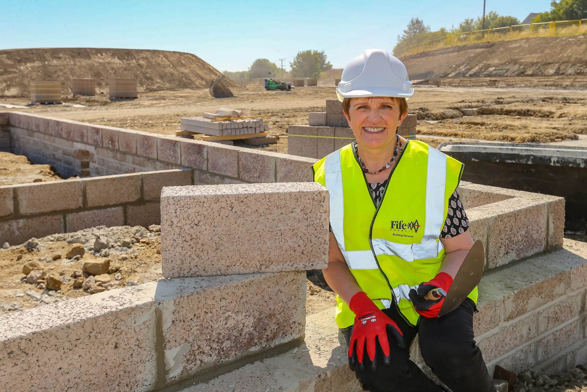 Councillor Judy Hamilton on a building site, wearing a hard hat and hi-vis vest.