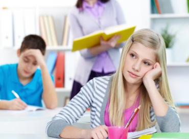 Girl with blonde hair sitting at a desk with her head in her hand