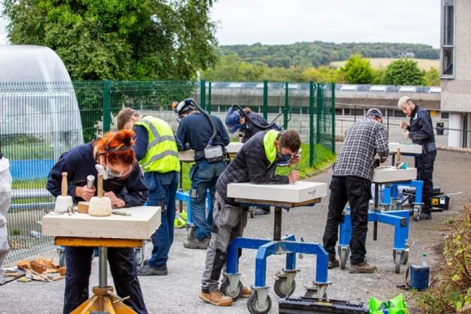 Seven young people in boilersuits and breathing filters carving slabs of stone while taking part in a traditional stone carving competition
