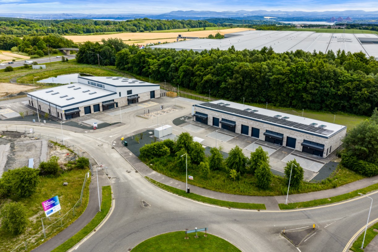 Fife Interchange North Aerial view of two modern industrial buildings with parking areas, surrounded by trees, fields, and roads.