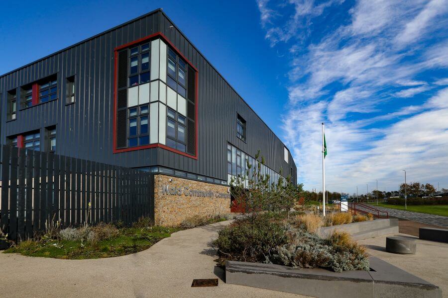 A view of Waid Community Campus from the side, with a flag and shrubs in the foreground