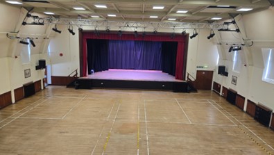 Main-Hall.jpg Empty hall with a wooden floor facing a stage with closed curtains