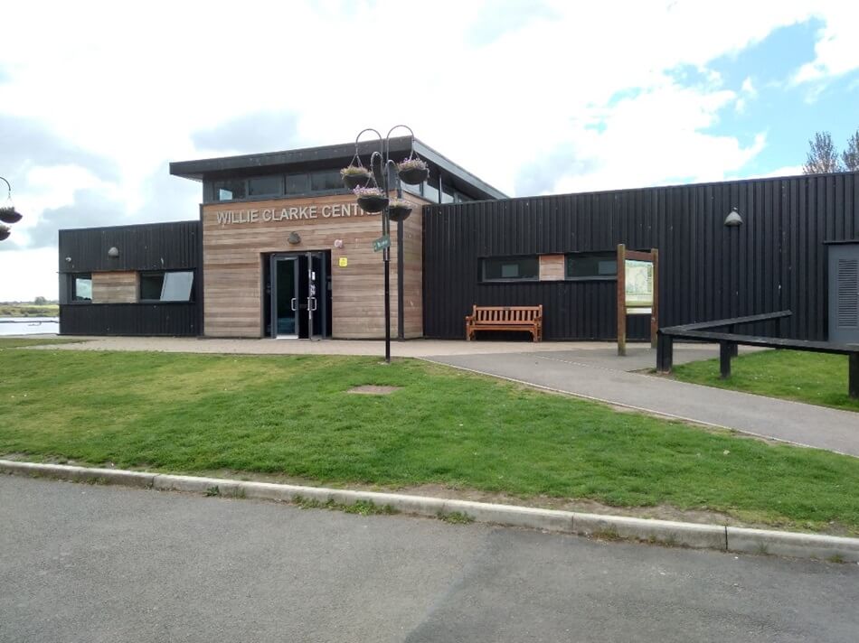 Willie Clarke Centre with wood and black panel exterior, surrounded by pathways, grass, and flower baskets to the front