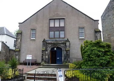 a stone memorial hall with a gabled roof, a large arched blue door, and small windows.