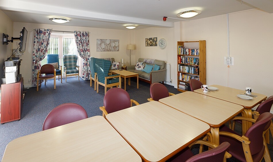Dining area at Meldrum Court with long table and chairs, and communal living room area to the rear