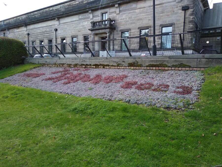 Red flowers arranged to spell 'Le Armistice 2023' in a garden bed in front of a stone building.