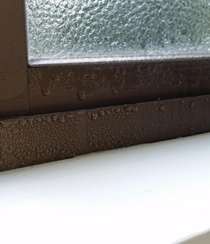 Condensation droplets on the inside of a window frame and sill.