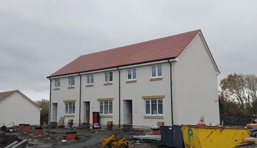 A row of terraced houses with white facades and red roofs, within a housing building site