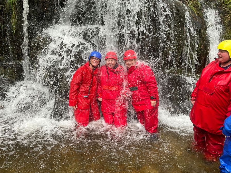 Three women in waterproofs standing under waterfall - Cash boost for summer programme across South and West Fife 