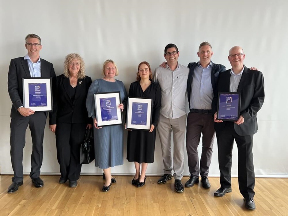 Seven of Fife's planning professionals stand together in a line against a plain backdrop. Four of the individuals hold framed certificates, marking national planning awards.