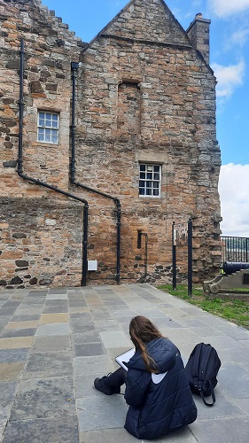 A pupil, with her back to the camera, sitting on the ground drawing outside the drawing for the Friary