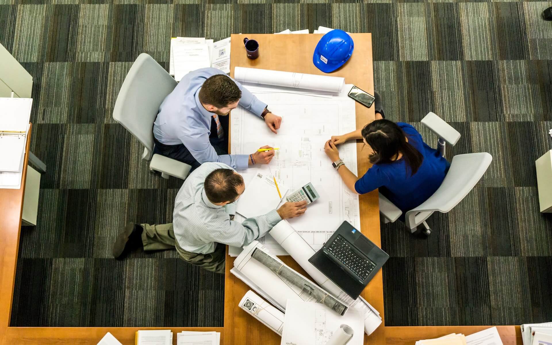 Aerial shot of three people sitting round a table with a laptop and plans