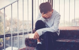 Young boy sitting on an outside step with his hand over his face and appearing to be upset