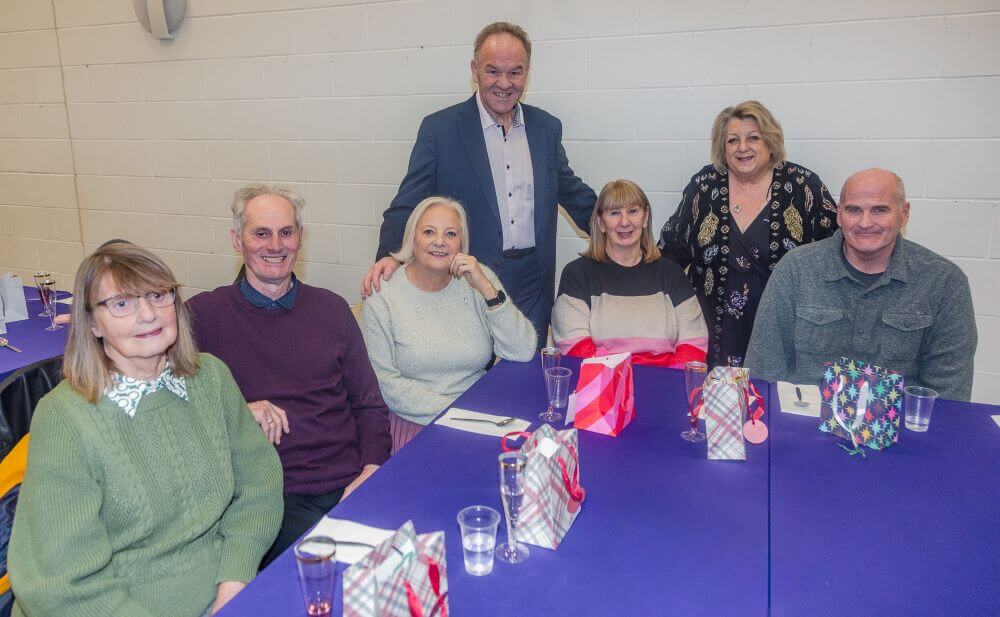 Cardenden Walking Club with Cllr Alex Campbell and Cllr Linda Erskine A group of eight people seated and standing around a table set with drinks and gift bags in a hall