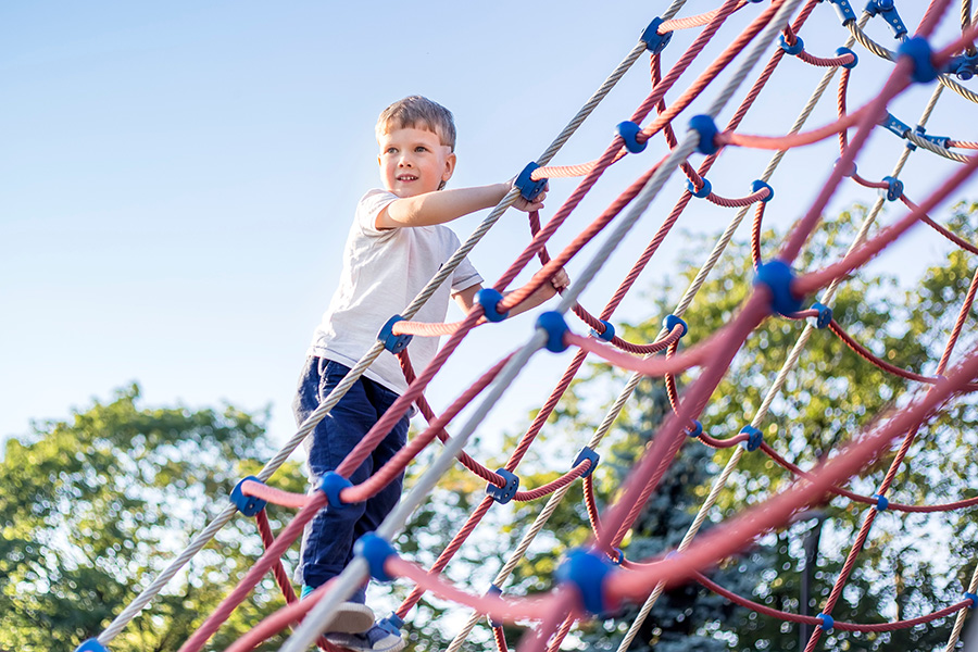 Kirkcaldy Area Committee agrees to help towards funding for new Kinghorn playpark Little boy wearing a white t-shirt and blue jeans climbing up a red and blue climbing net
