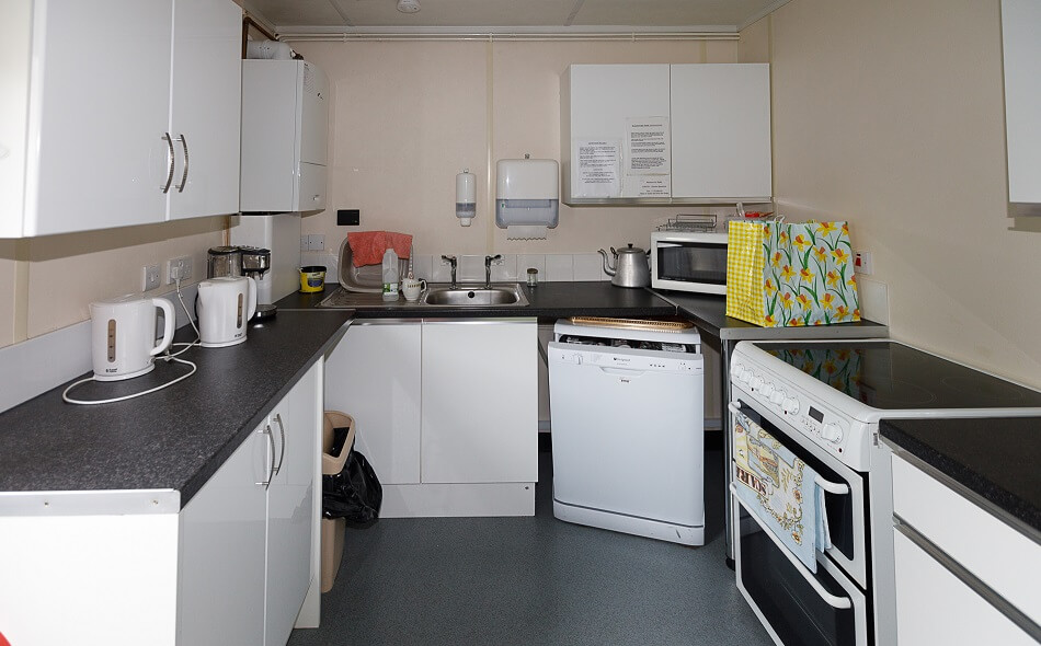 Communal kitchen with white cupboards and grey table top. Kitchen has a cooker, dishwasher, sink and two kettles