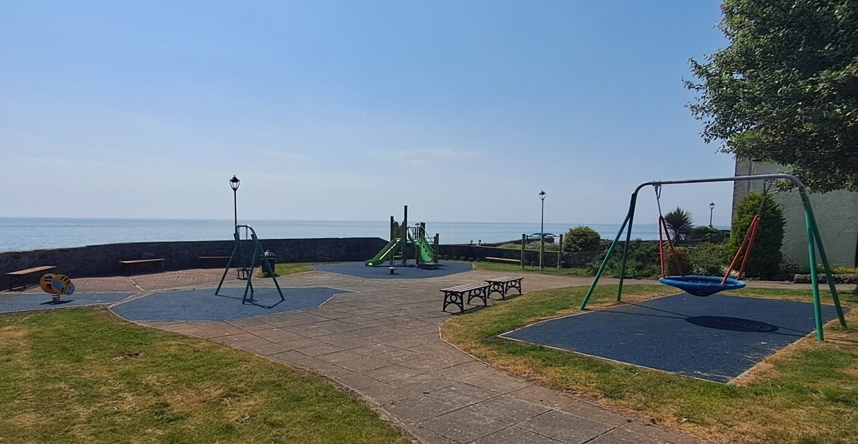 A playground with swings, slides, and climbing equipment. The playground is located by the water