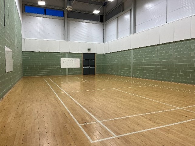an indoor gymnasium with a polished wooden floor, green brick walls, basketball hoops, and whiteboards