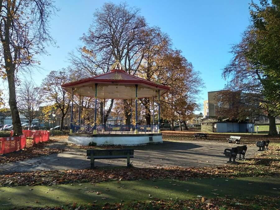 Red-roofed bandstand in Haugh Park with benches and fallen leaves