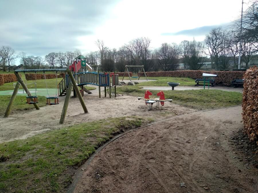 Playground in Haugh Park with swings, slides, and a red horse seesaw among trees.