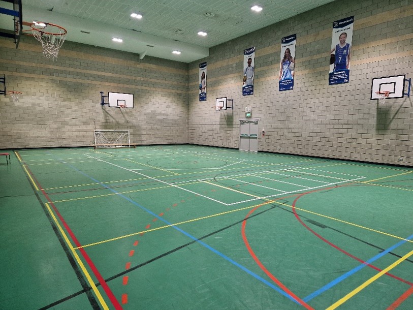 An empty indoor muti-purpose basketball court with four hoops, a small goal, and four banners featuring athletes hanging on the far wall.