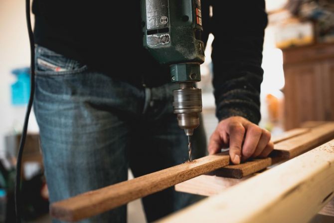 zoomed in image showing someone drilling a hole in a length of wood, with an electric drill