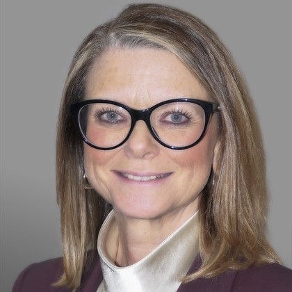Elaine Muir Formal head‑and‑shoulders portrait of Elaine Muir wearing dark-framed glasses, a dark jacket and a light blouse, photographed against a plain grey background.