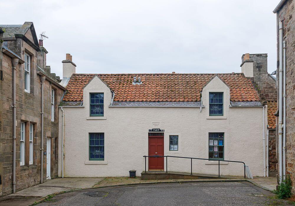 Front view of a small, traditional building with a red tiled roof and central doorway, identified as a museum, set between stone buildings on a quiet street. The entrance has a ramp with handrails, and the windows display signage. - Funding approved to help preserve Crail’s historic Sea Box records