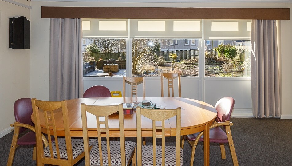 Communal lounge at Sunnyside Court, with dining table facing views of the gardens outside