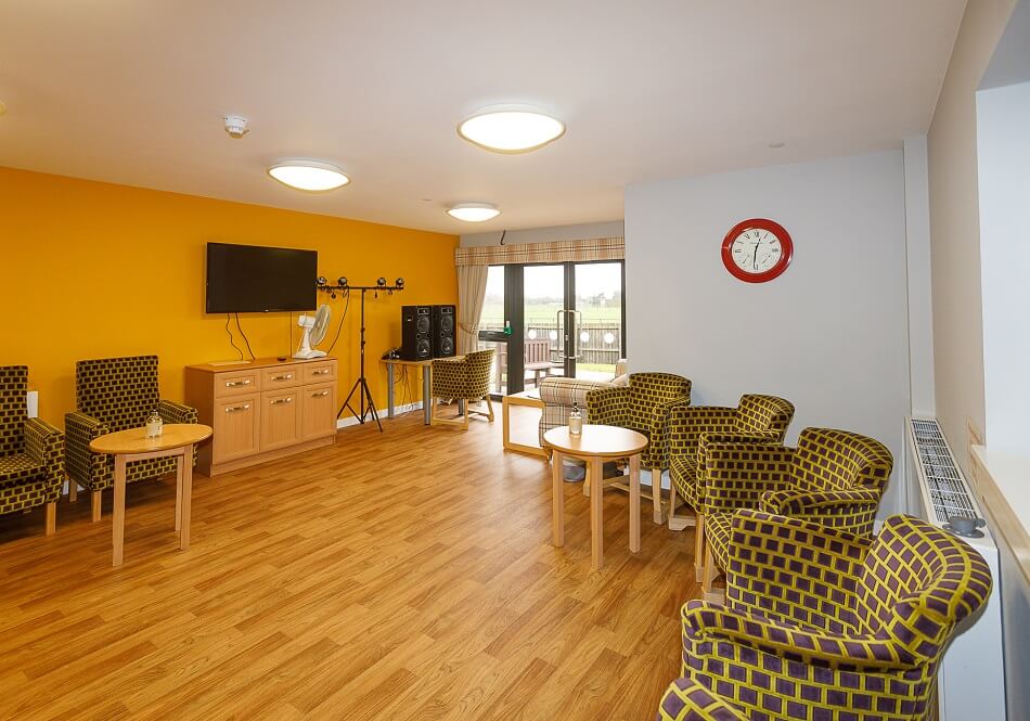 Communal seating and TV area at Cedar House, with bright yellow walls and patterned seats