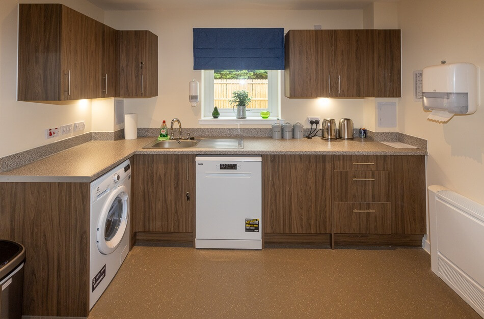 Communal kitchen with brown wood doors and white appliances, looking out of the window to the garden
