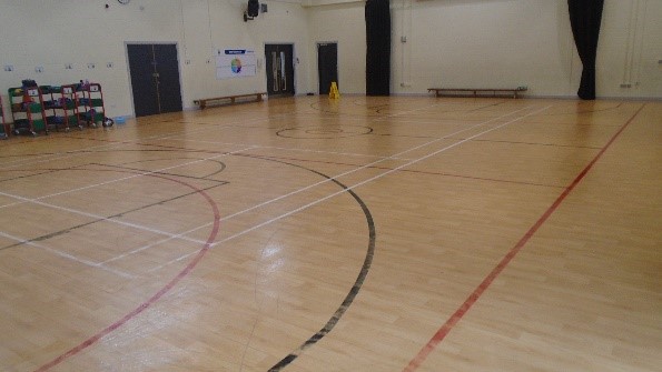A bright, empty sports hall. The floor has many court lines. Benches line the far walls.