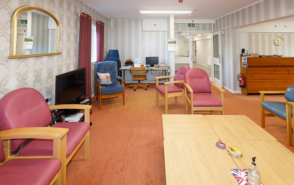 Communal seating area at Moir Court, with armchairs and a coffee table facing a TV, taken from another angle