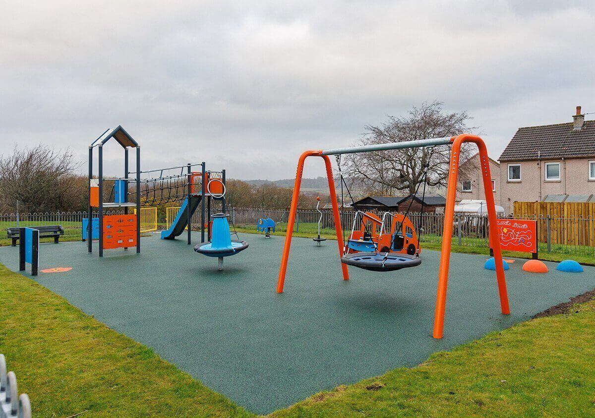 Modern outdoor play park with swings, a climbing structure, a slide, and bright orange and blue equipment set on a soft play surface