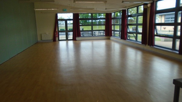 An empty hall. It has a wooden floor and large windows