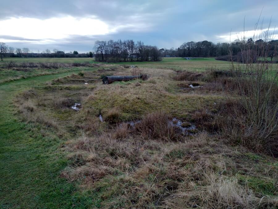 A marshy, uneven grassy area in Dunnikier Park with small burn