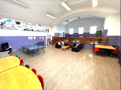 A colourful room with a table-tennis table, desks and comfortable seating