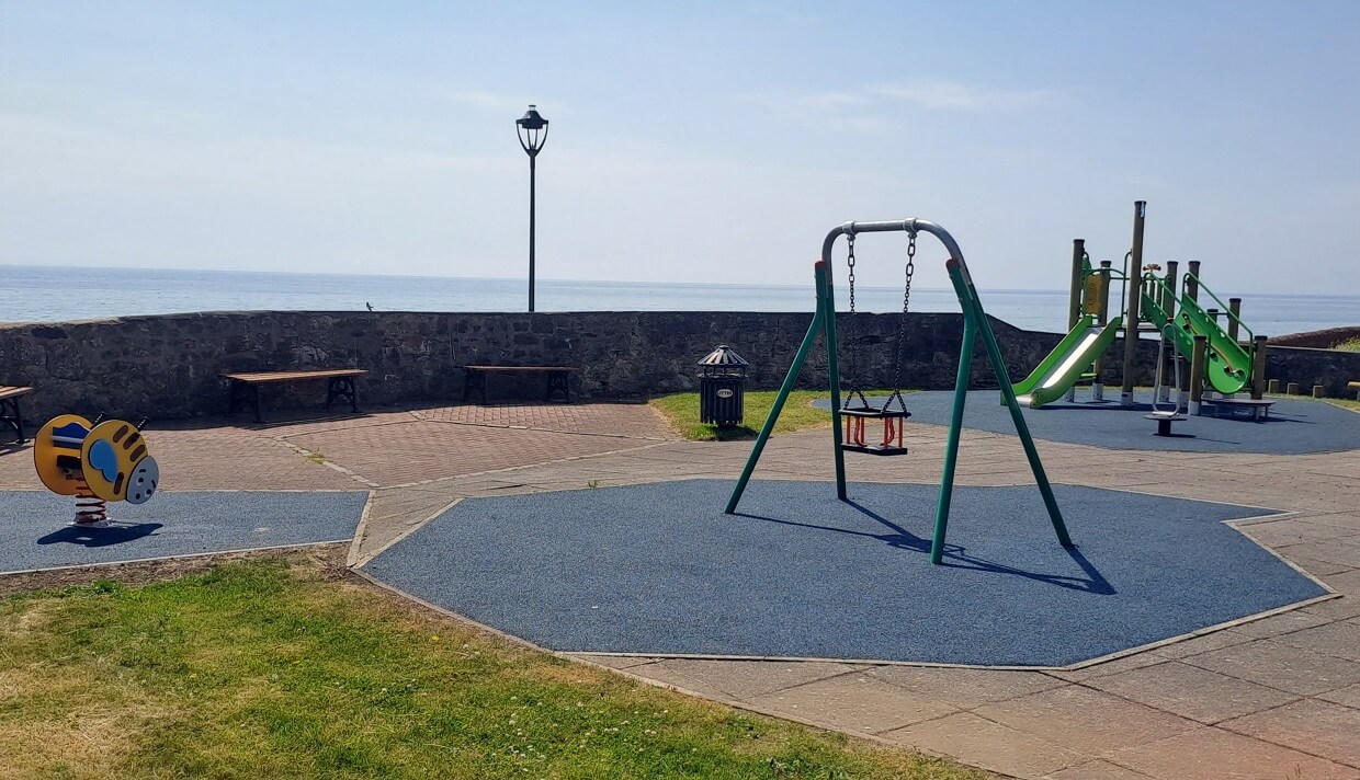 A playground with swings, slides, and climbing equipment. The playground is located by the water