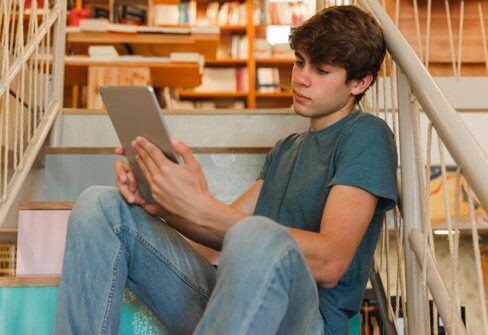 Teenage boy with brown hair sitting on a set of stairs and looking at a tablet device