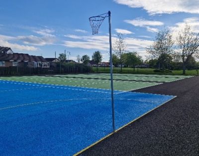 A blue and green outdoor sports court with a Netball court in foreground and tennis court in background