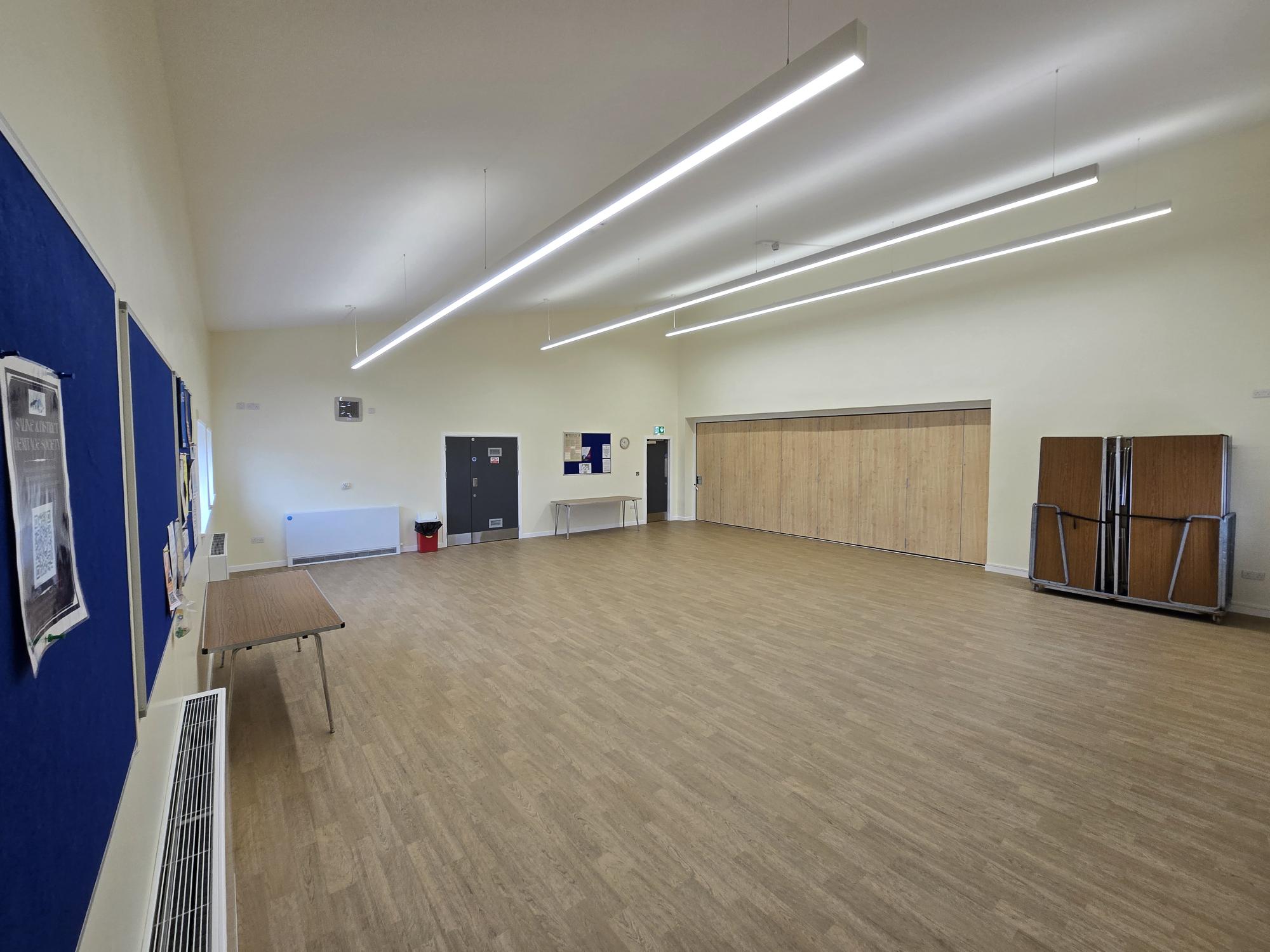 Saline-CC-Small-Hall.jpg Empty community hall with wooden floor and strip lighting