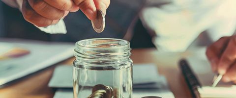 person putting coin into a jam jar