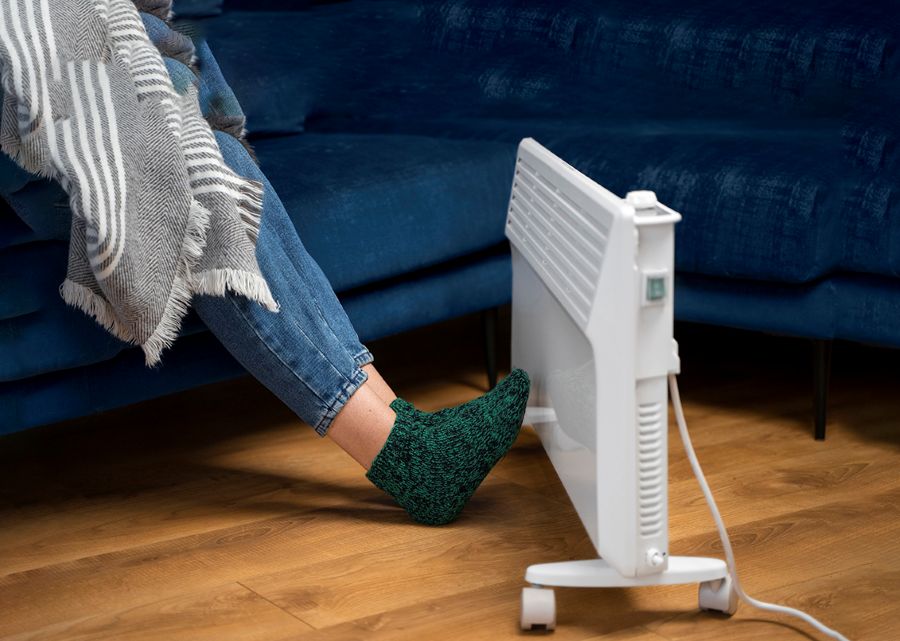 Women wrapped in blanket, sitting on couch warming feet at a radiator