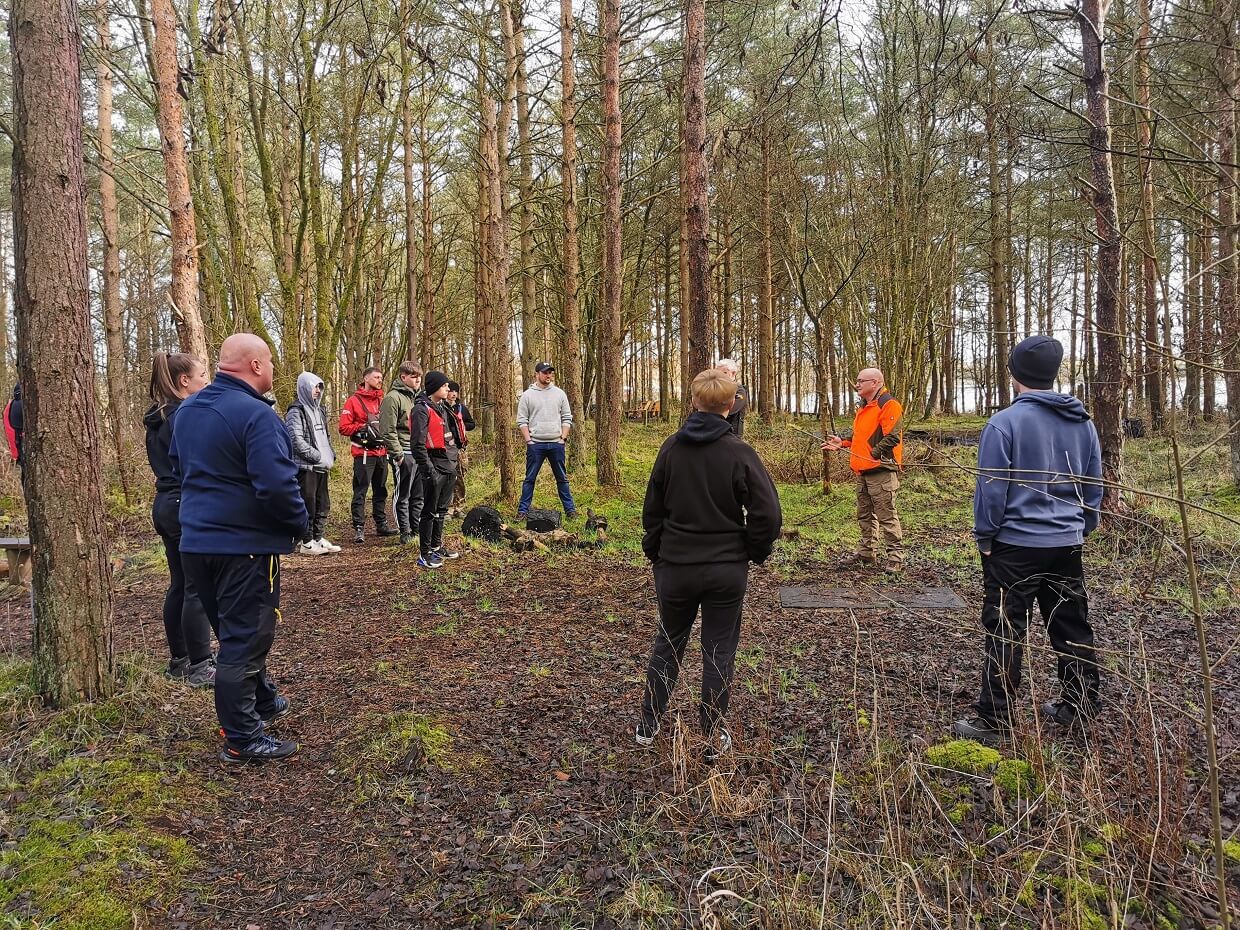 a roup of people standing in a circle in the woods