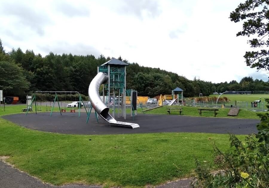 Playground at Gilvenbank Park with slide, swings, and climbing structure, surrounded by grass and trees
