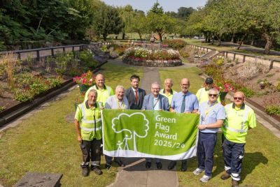 Councillors and staff holding the Green Flag award flag with Letham Glen's beautiful and colourful sunken garden  in the background