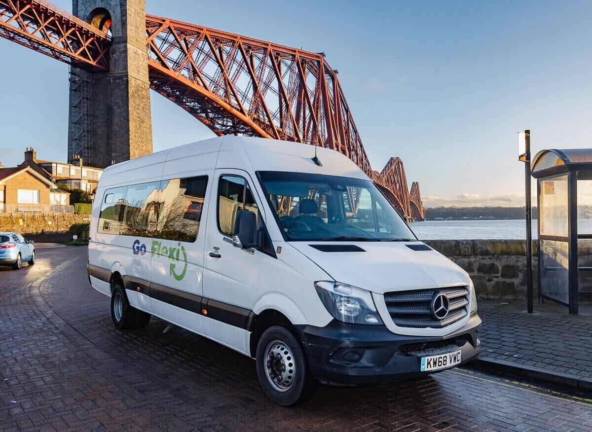 White Go Flexi minibus parked beside the waterfront with the Forth Bridge in the background.