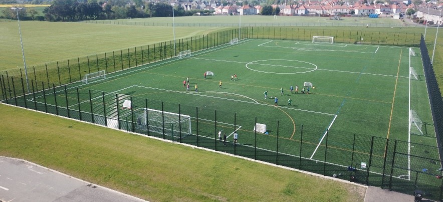  An aerial view of a fenced artificial football field with players