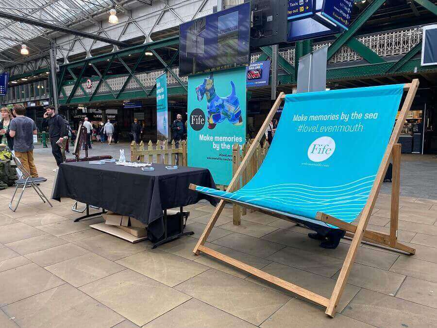 An oversized chair next to a table and Fife poster at the Expo
